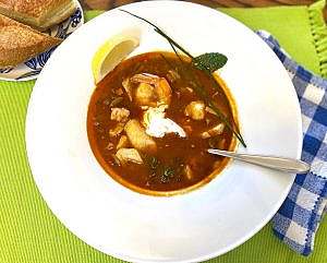 Hungarian fish soup with sour cream topping, garnished with chives, mint, and parsley.
