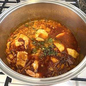 Hungarian fish soup simmering with shrimp, white fish, herbs in red broth.