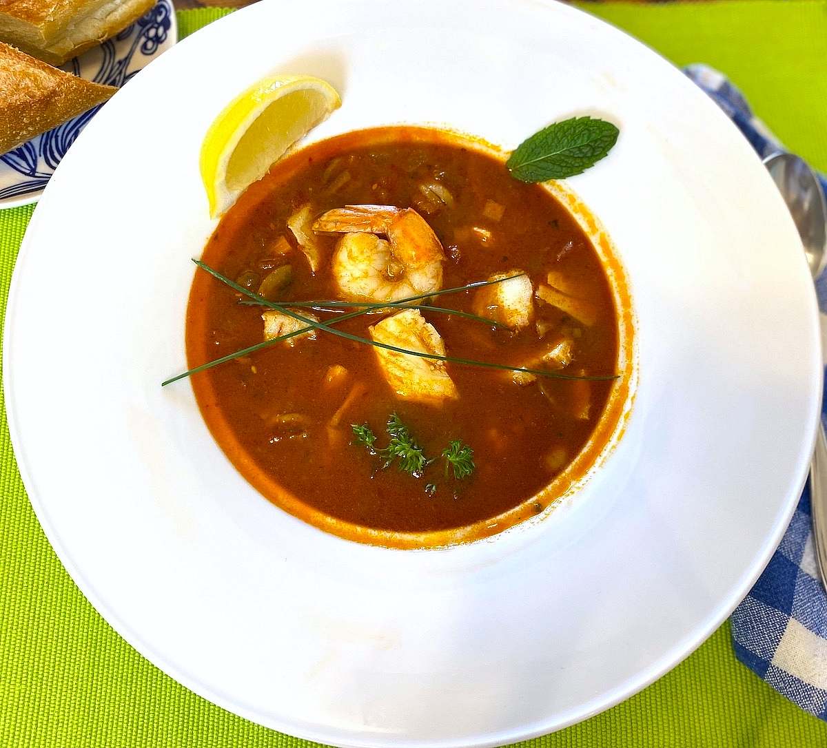 Hungarian fish soup with shrimp and fish, garnished with lemon, chives, mint, and parsley.