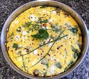 Freshly baked Mediterranean frittata in a stainless steel skillet, topped with herbs and red pepper flakes.