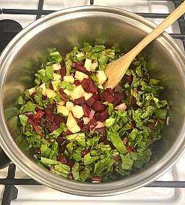 Pot filled with chopped beets, beet greens, and potatoes beginning to sauté on the stovetop.