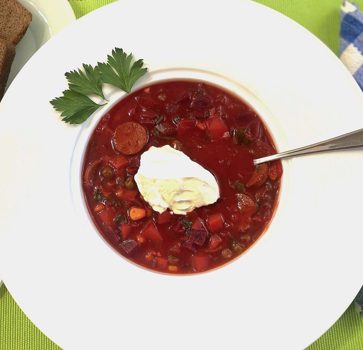 Close-up of a bowl of vibrant red borscht showing beets, vegetables, sausage, and creamy topping.
