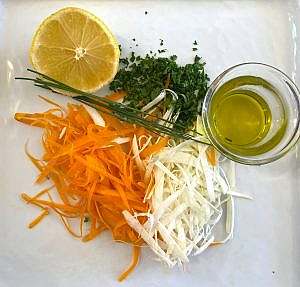 Close-up of julienned carrot and parsnip with lemon half, olive oil, parsley, and chives ready for garnish.