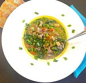 Close-up of a white bowl filled with vegetable curry spicy soup with vegetables and noodles, served with a spoon and ready to eat.