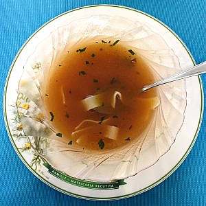 Light tomato noodle soup garnished with parsley in a small bowl.