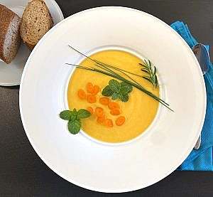Silky carrot parsnip potato soup garnished with fresh herbs and olive oil, served warm in a white bowl